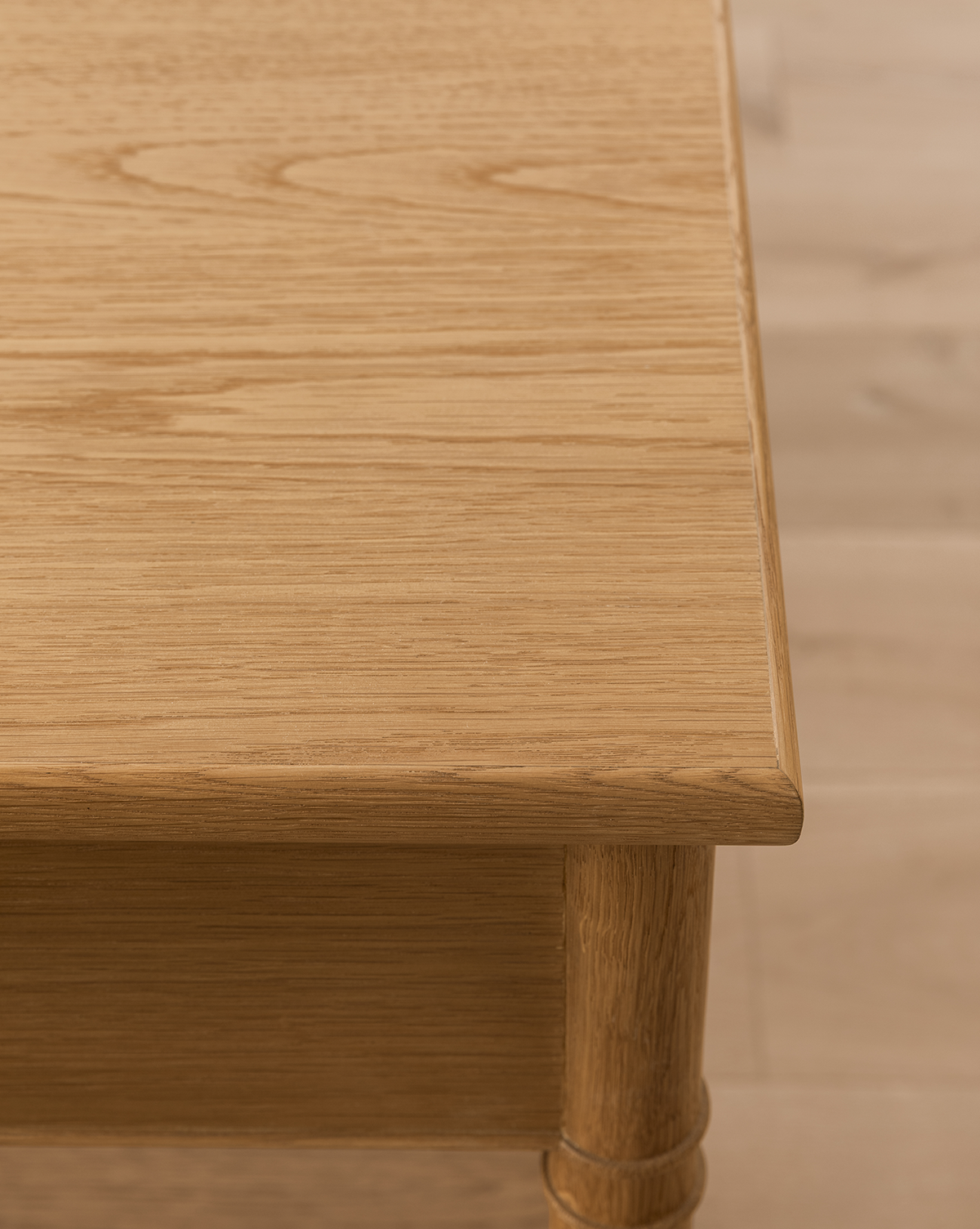 Close-up of the Hindley Console, featuring a smooth, light oak finish on the tabletop and rounded leg, set against a light wood floor background, by McGee & Co.