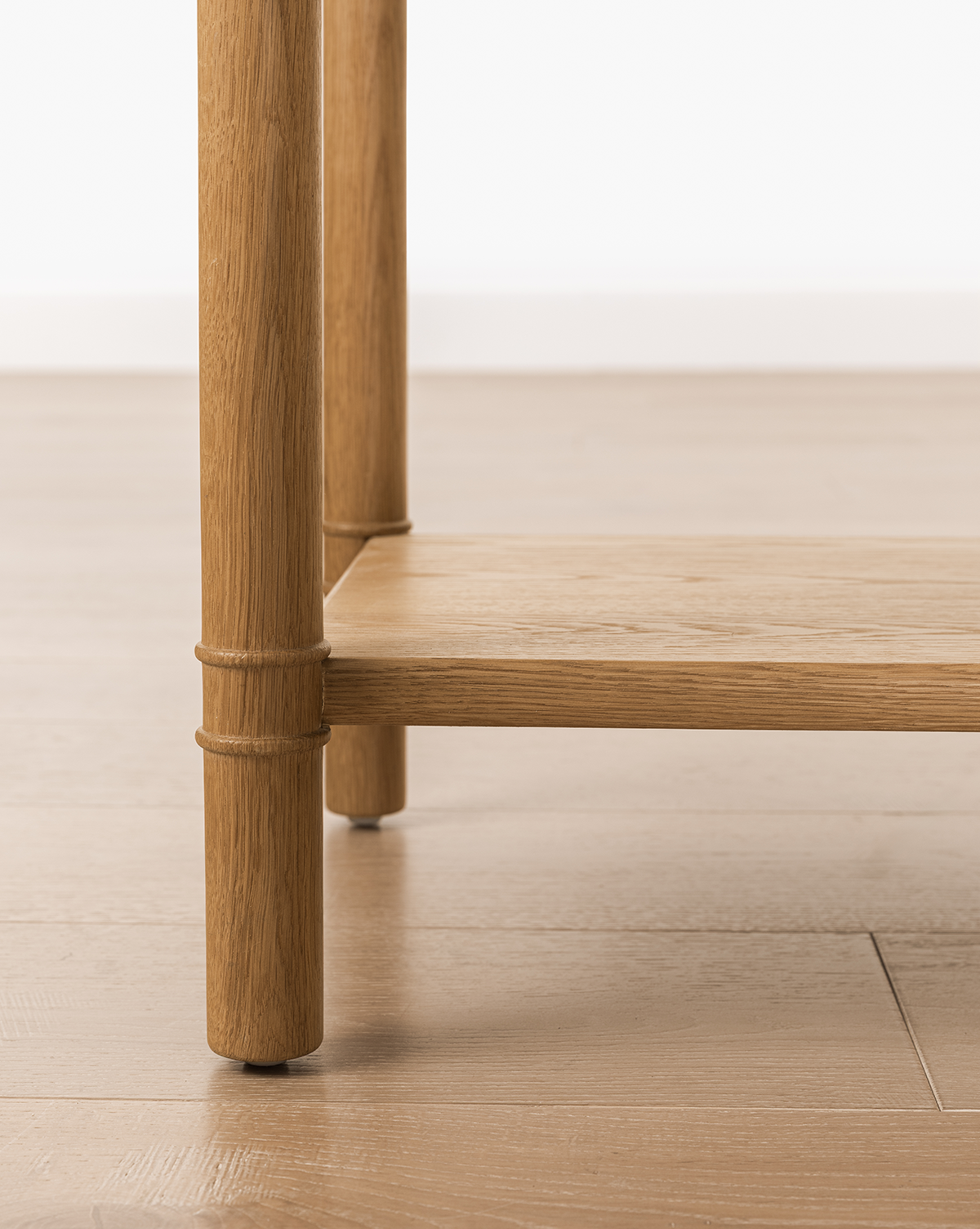 Close-up of the Hindley Console's oak leg and lower shelf on a light wood floor, showcasing its smooth finish and natural grain—perfect as a stylish entryway table, by McGee & Co.