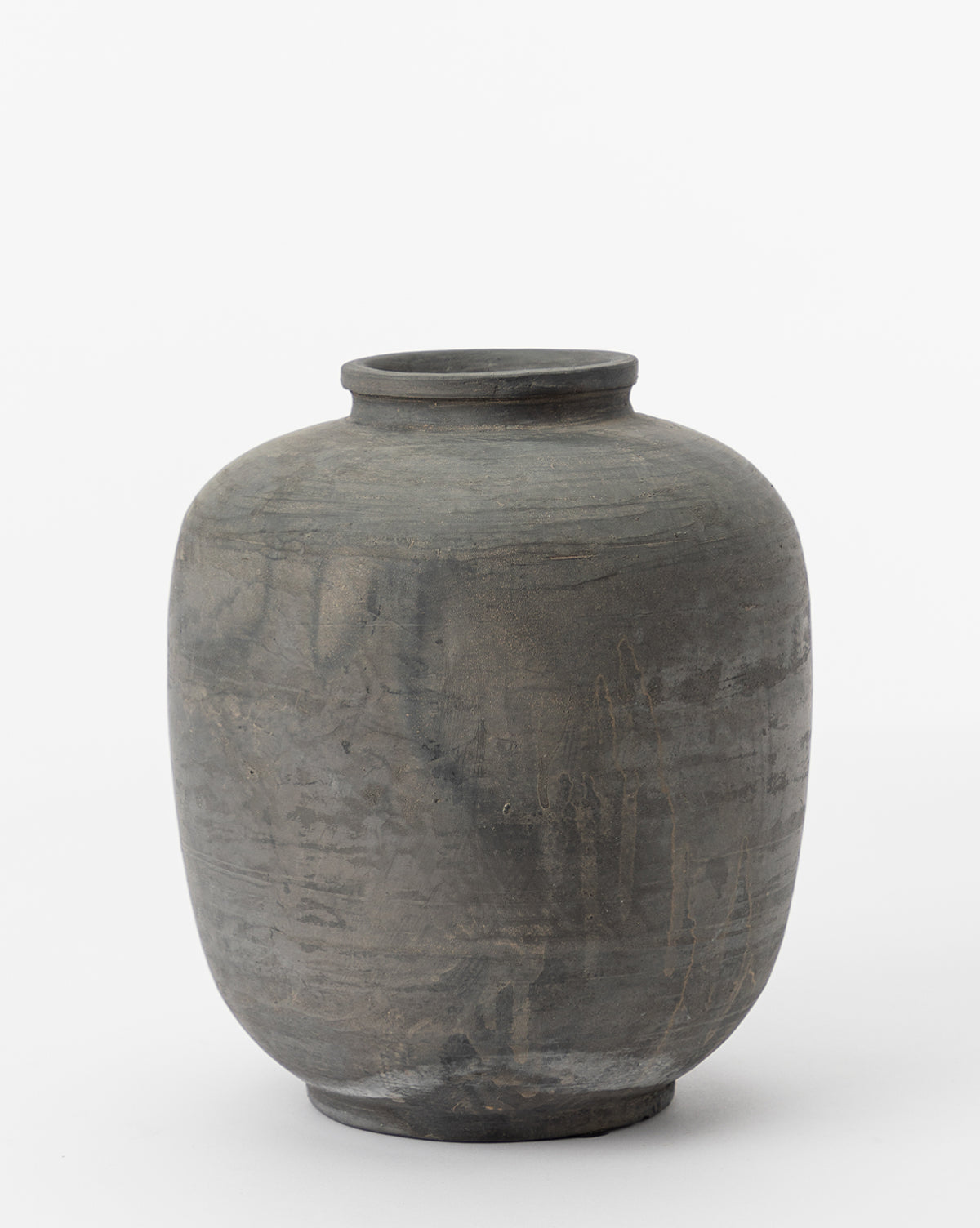 The Jexa Vase is a round, dark gray ceramic piece with earthy tones, a narrow flared neck, and a smooth textured surface, shown against a plain white background.