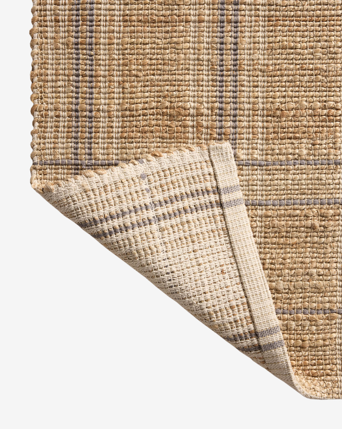 Close-up of a handwoven rug in tan and beige plaid, with one corner turned to show the pattern and natural, coarse texture—styled like the Judy Jute Rug Collection No. 2, by McGee & Co.