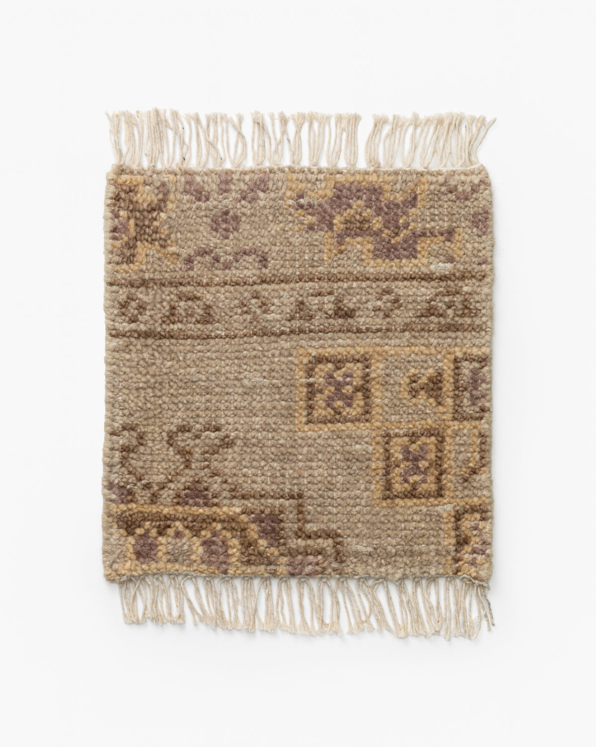 The Kenna Hand-Knotted Wool Rug Swatch is a small, rectangular wool piece featuring beige and brown geometric and floral patterns, tasseled fringe on two ends, and a textured, slightly worn look by McGee & Co.