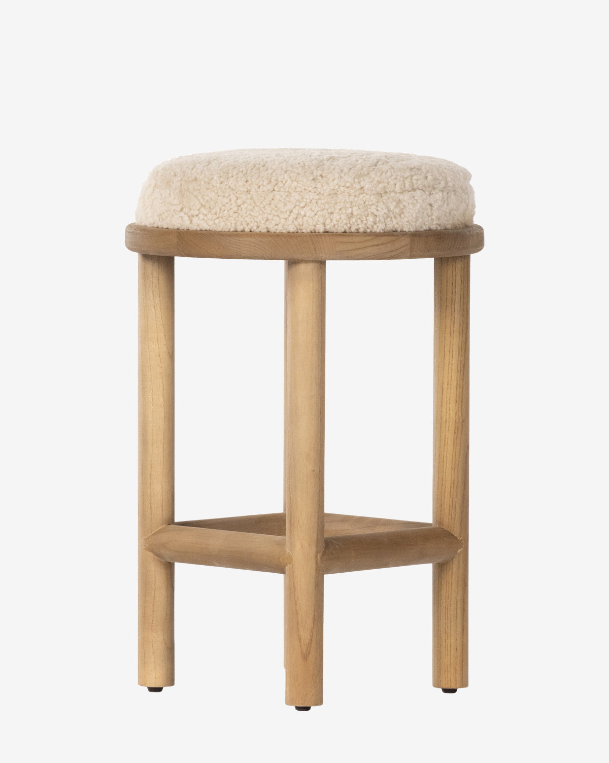 The Linus Stool has four wooden legs and a round, cushioned seat upholstered in soft beige shearling, making it ideal for comfortable counter seating, by McGee & Co.