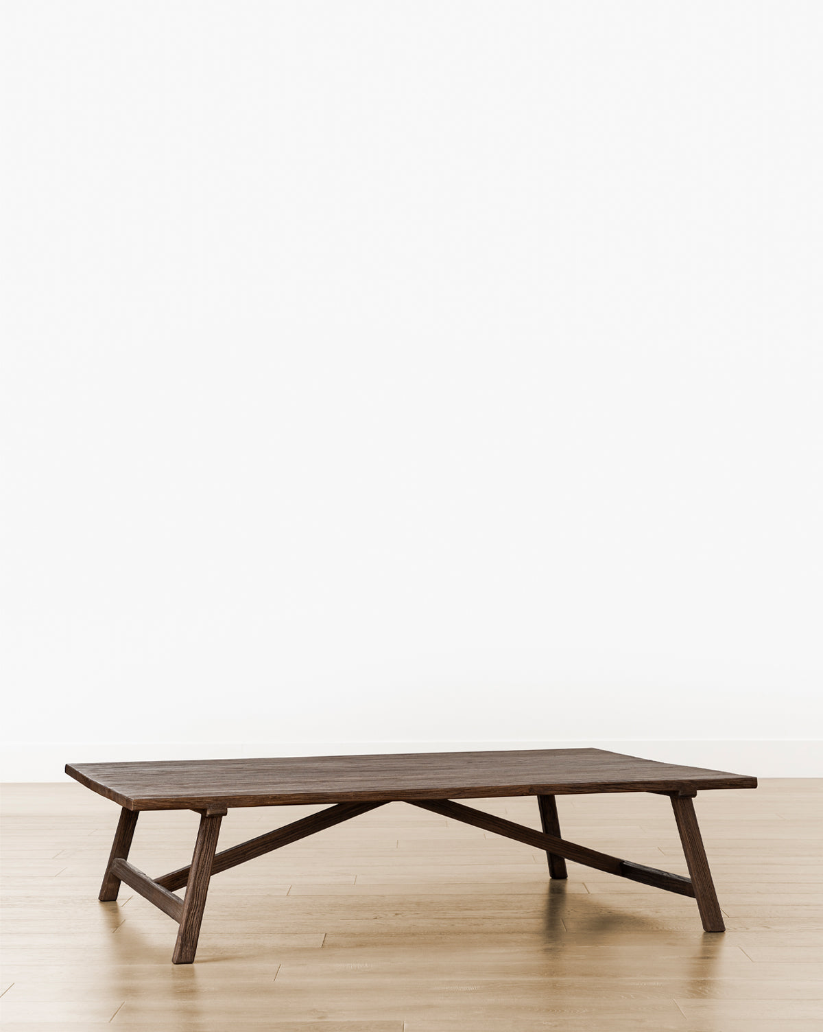 The Lockwood Coffee Table, a low rectangular piece made of English Oak with angled legs, stands on a light wood floor against a white wall, creating a minimalist and modern look, by McGee & Co.