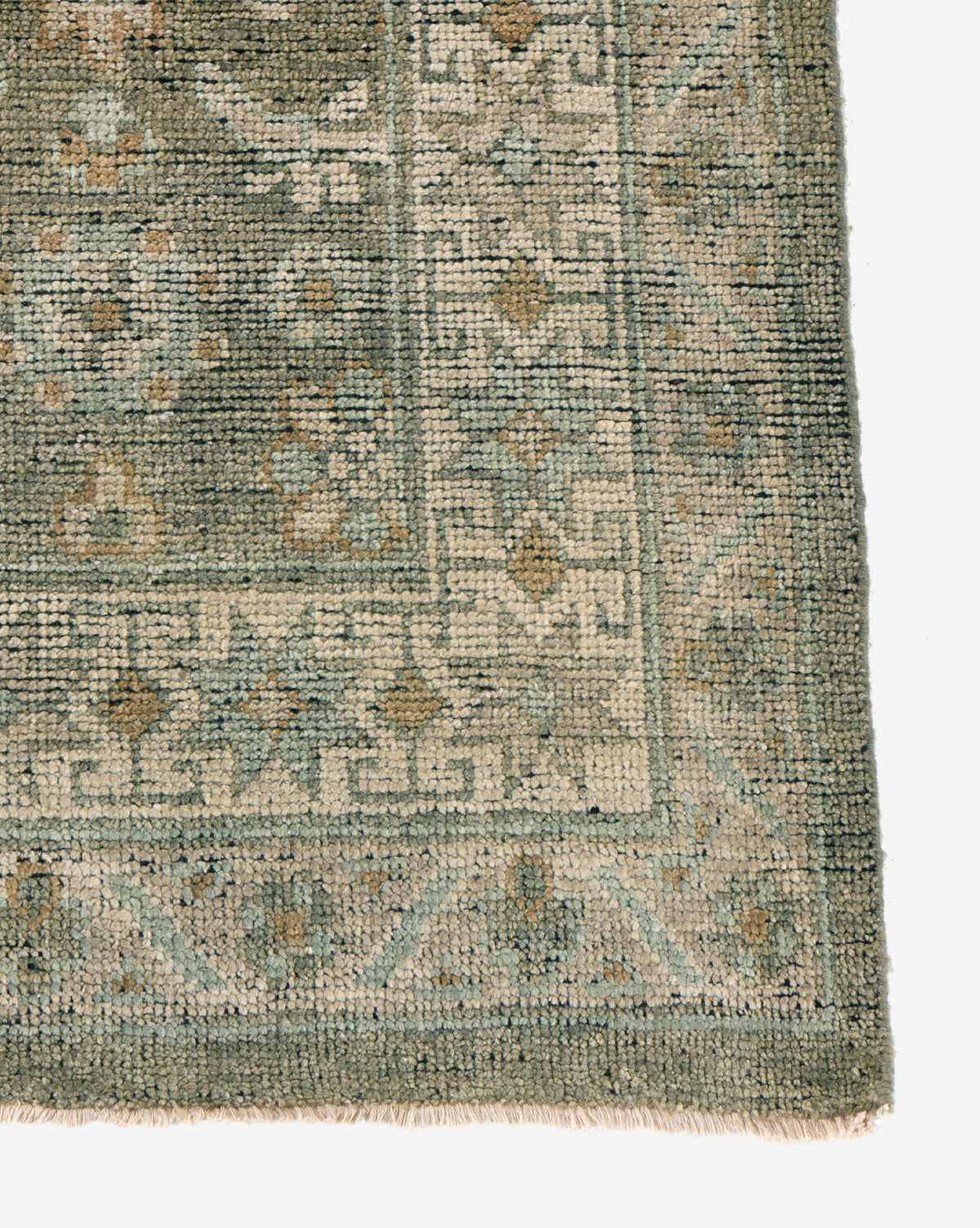 A close-up of the Loreo Hand-Knotted Wool Rug's corner reveals a geometric and floral border in green, beige, and light blue. The visible texture and short fringe showcase the quality craftsmanship of this earth-tone rug, by McGee & Co.