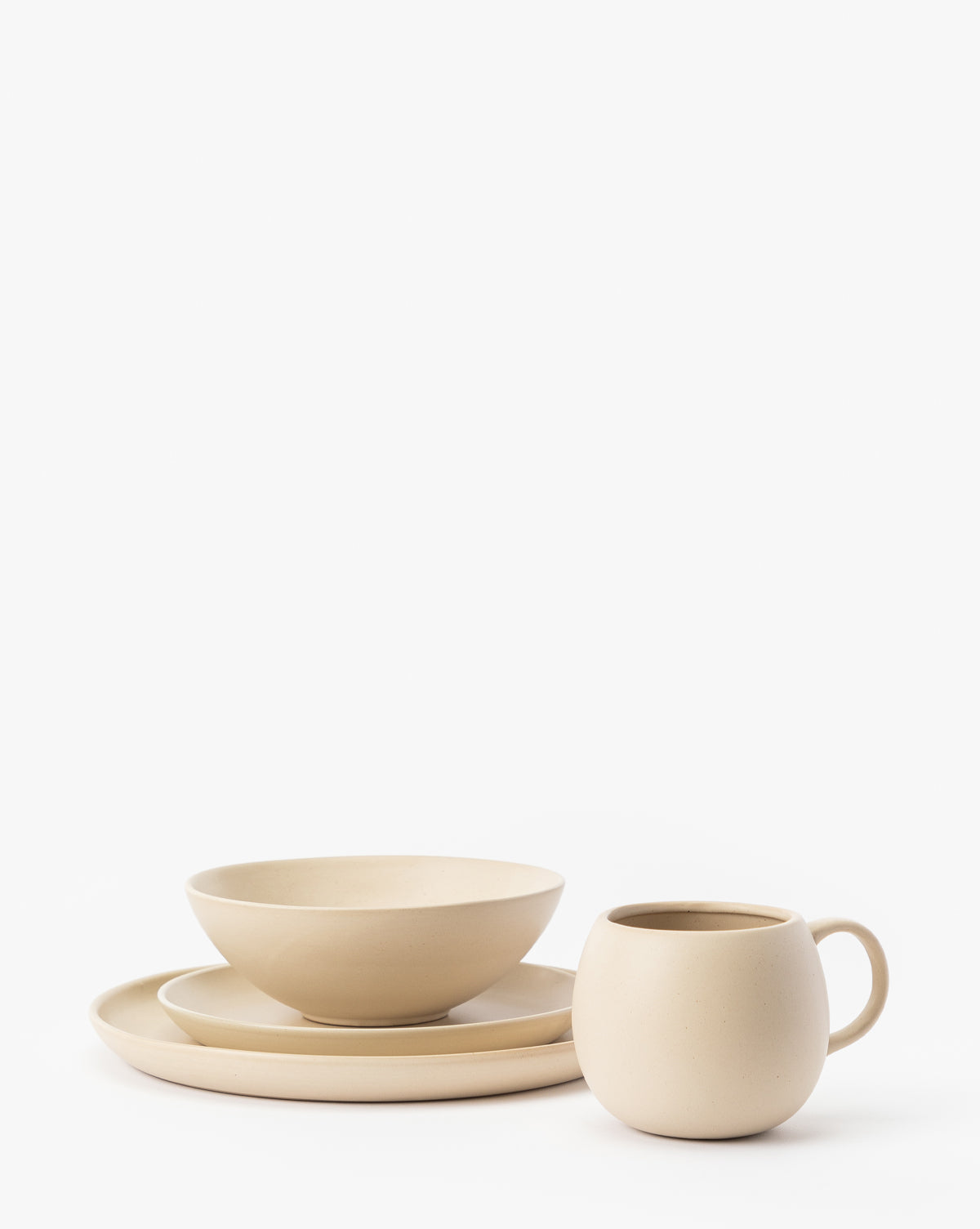 A modern beige stoneware dinnerware set featuring the Luana Bowl, a round plate, and a handled mug—all displaying a neutral palette and arranged on a white background, by McGee & Co.