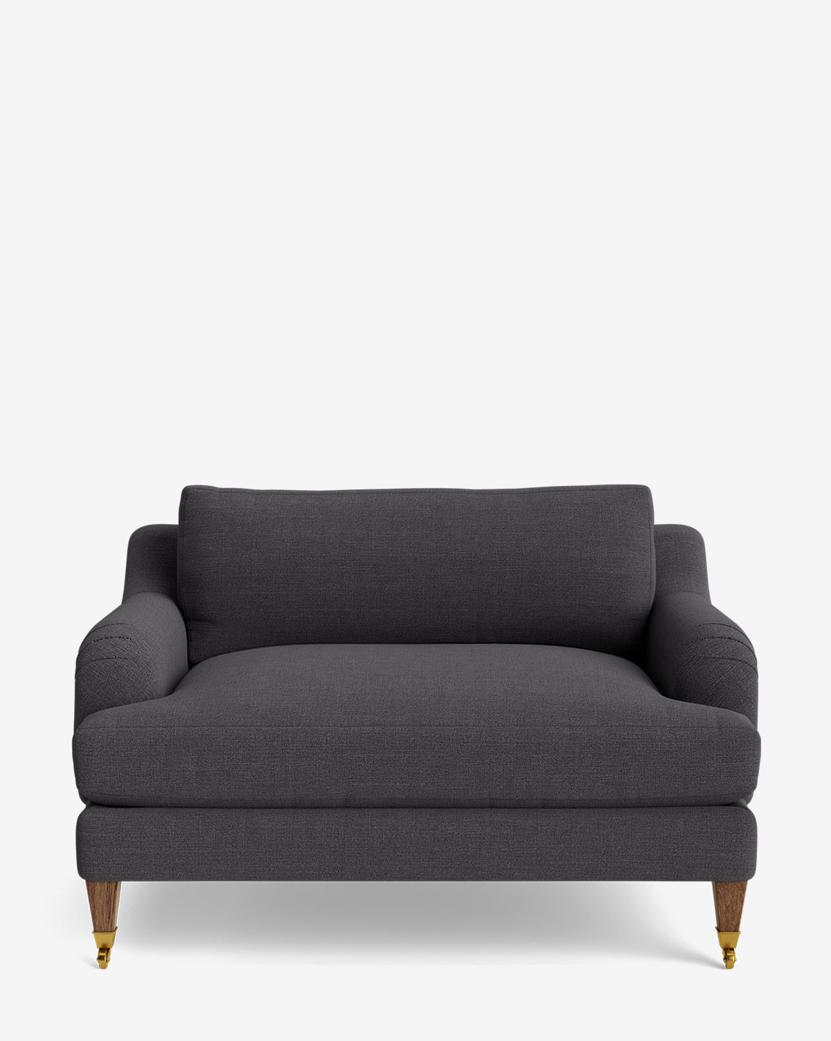 The Lucille English Roll Arm Chair and a Half is a dark gray, upholstered seat with English roll arms, a cushioned backrest with down wrapped cushions, and wooden legs—two with brass casters—shown on a plain white background by McGee & Co.