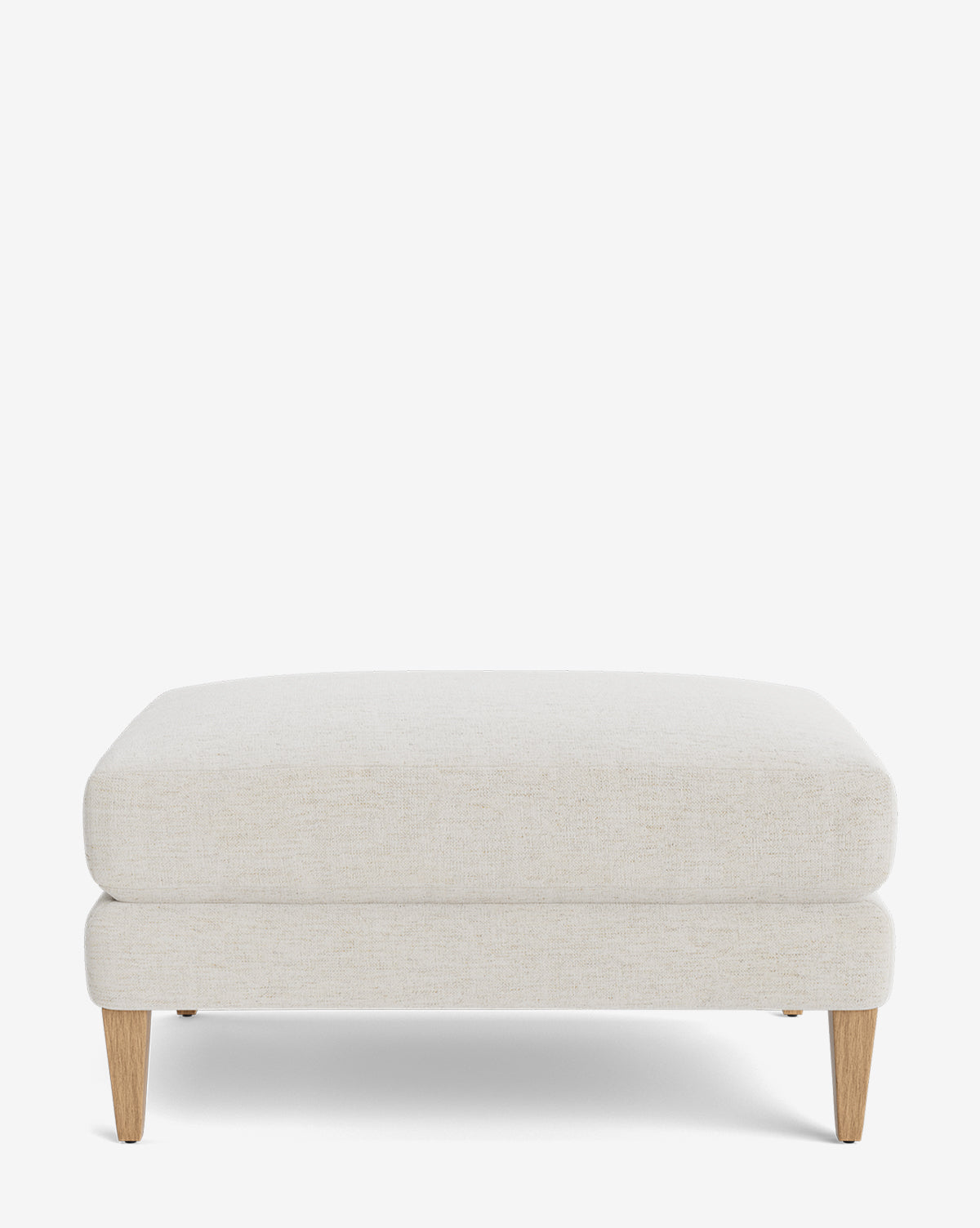 The Lucille Ottoman features a modern rectangular design with light beige upholstery and four angled wooden legs. Shown against a white background, this customizable piece blends style and versatility for any room by McGee & Co.