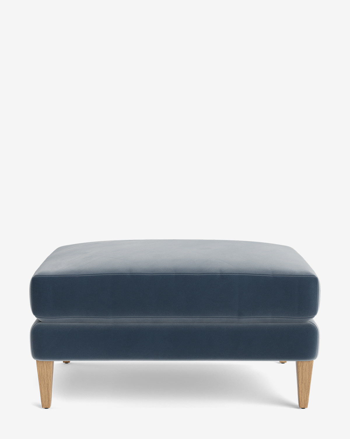 The Lucille Ottoman is a modern rectangular blue velvet piece with light wooden tapered legs, displayed on a plain white background—perfect for adding style and comfort to any space, by McGee & Co.