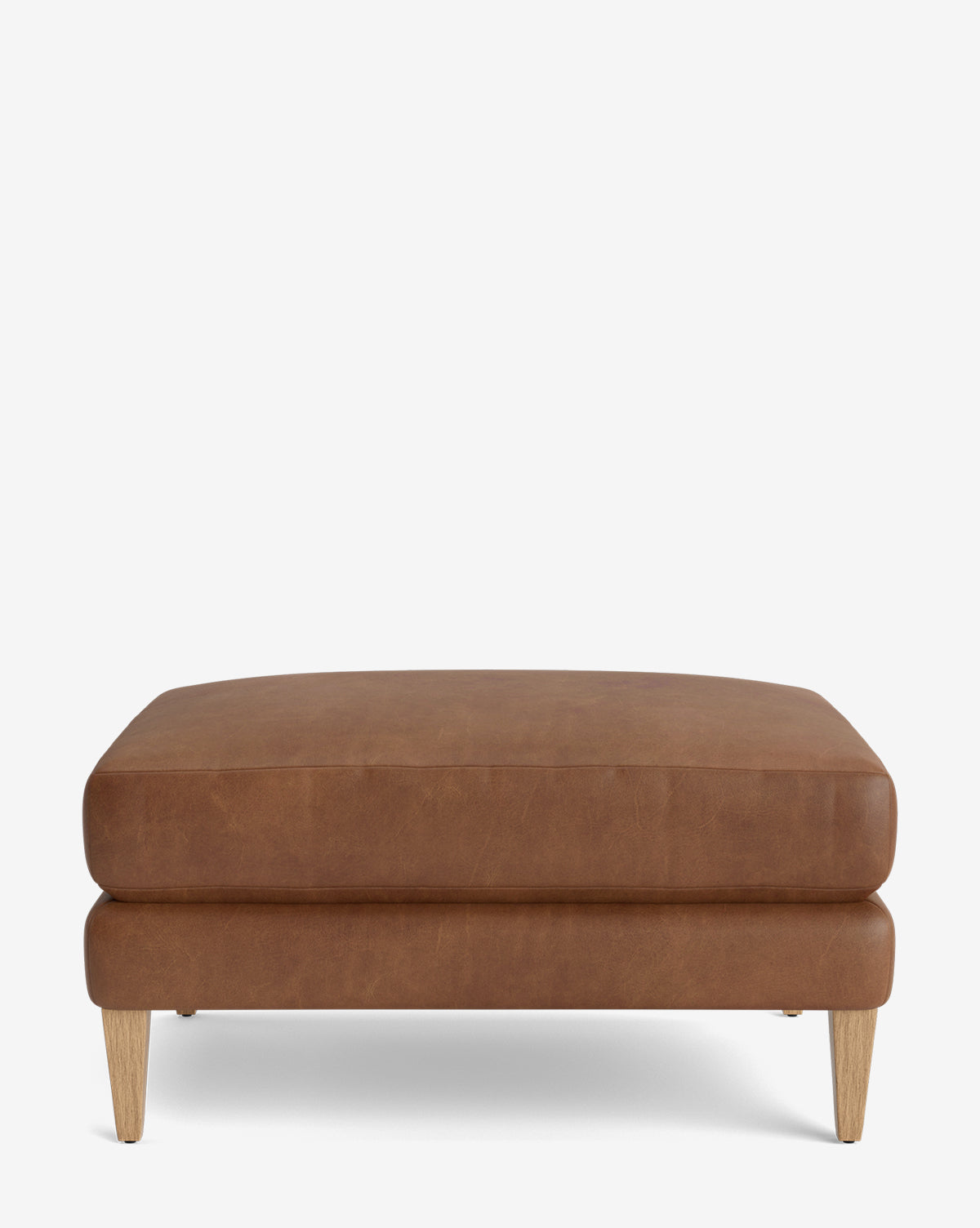The Lucille Ottoman features a minimalist, modern design with a rectangular brown leather seat and wooden legs. It is customizable and displayed against a plain white background, by McGee & Co.