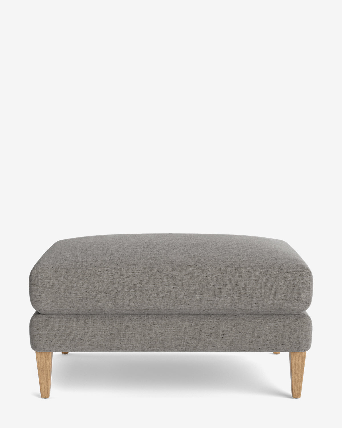 The Lucille Ottoman is a customizable rectangular grey upholstered ottoman with light wooden tapered legs, shown against a plain white background—a modern, versatile piece for any room, by McGee & Co.