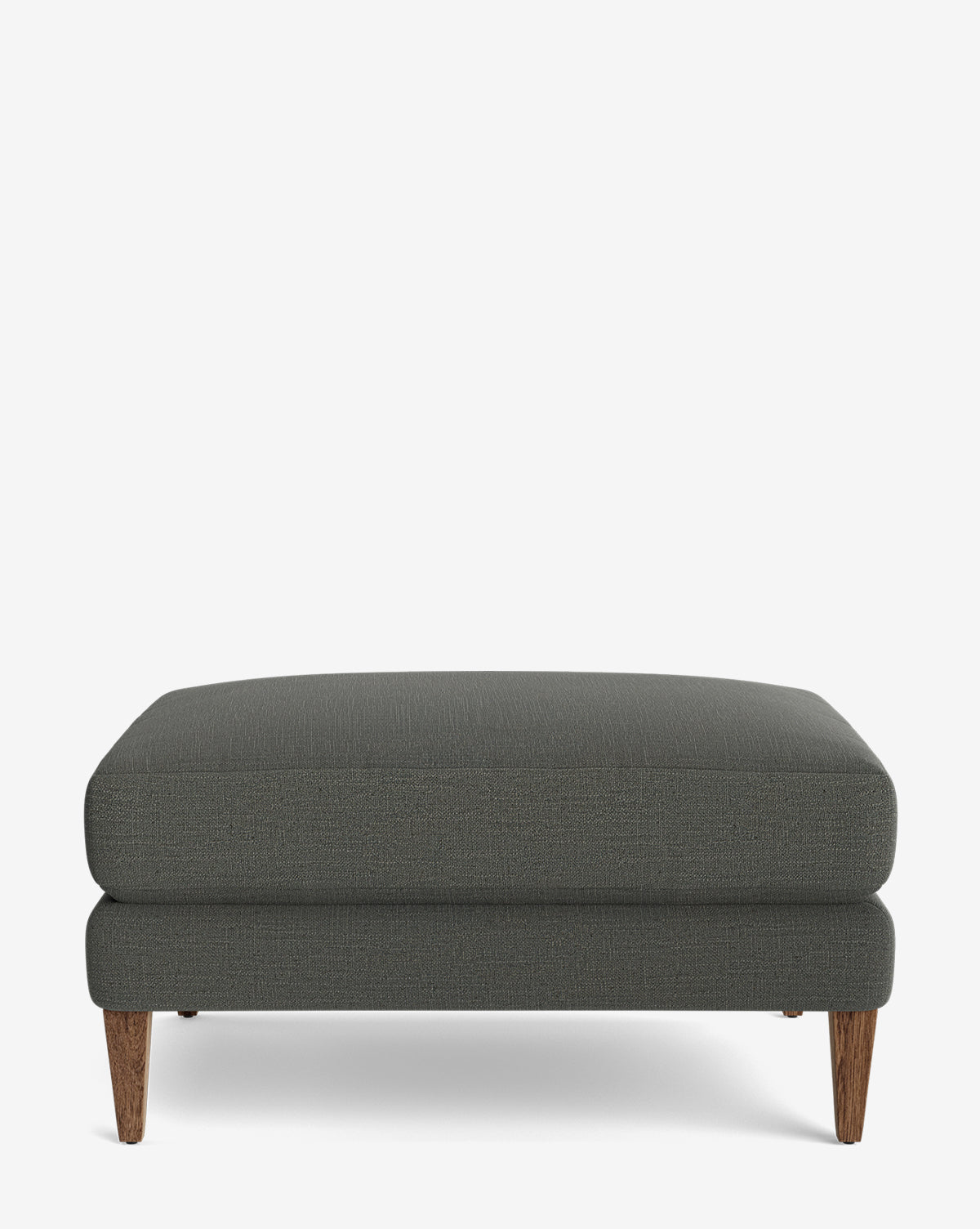 The Lucille Ottoman is a modern rectangular piece with dark gray upholstery and four angled wooden legs, displayed on a white background, by McGee & Co.