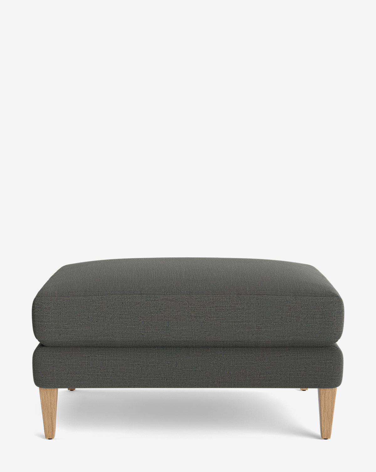 The Lucille Ottoman features a modern rectangular design with dark gray upholstery and wooden legs, displayed on a plain white background, by McGee & Co.