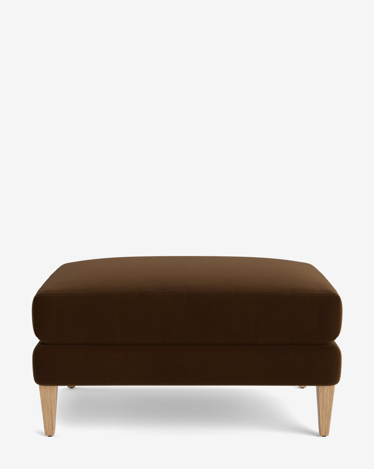 The Lucille Ottoman is a modern rectangular ottoman with a cushioned top, dark brown upholstery, and four light wood legs, shown on a plain white background by McGee & Co.
