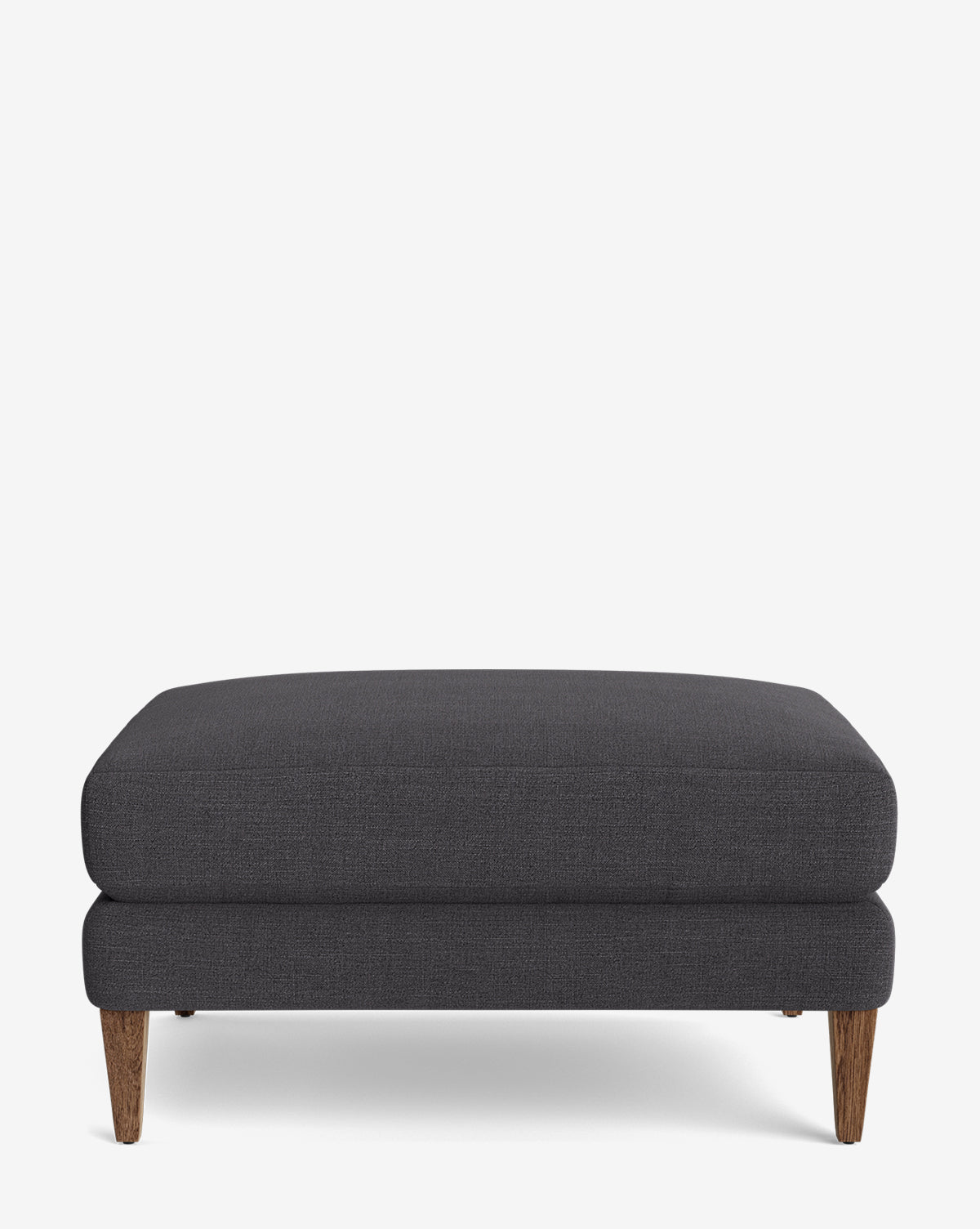 The Lucille Ottoman features a modern, minimalist rectangular design with dark gray upholstery and angled wooden legs, shown on a plain white background by McGee & Co.
