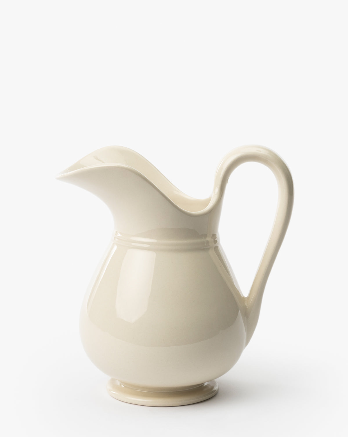The Lumen Pitcher is a cream-colored stoneware piece with a curved handle, wide spout, and smooth white finish, shown on a plain white background, by McGee & Co.