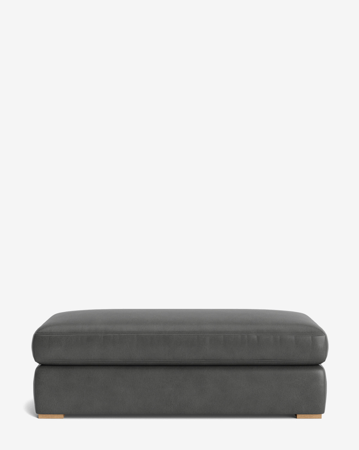 The Macy Upholstered Ottoman is a modern, rectangular piece in dark gray with a smooth surface and low wooden feet, ideal for living room furniture and shown against a plain white background, by McGee & Co.
