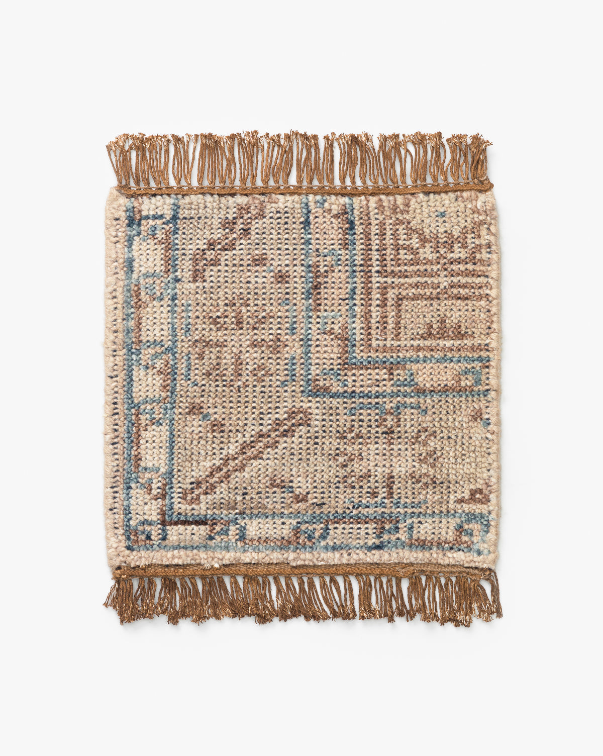 The Nunez Hand-Knotted Wool Rug Swatch features a small rectangular shape, brown and blue geometric patterns on a cream background, hand-knotted wool construction, and fringed edges on two sides, shown on a white surface by McGee & Co.