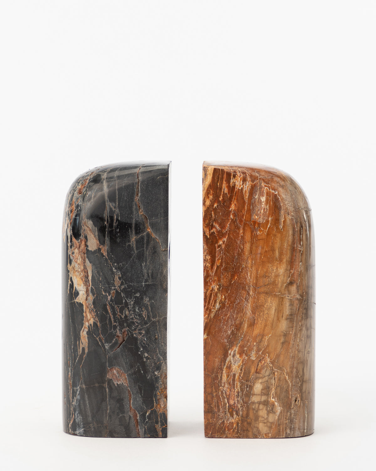 The Petrified Wood Bookends (Set of 2) feature smooth, rounded sculptures in black with brown and white veining and reddish-brown with lighter streaks, polished to perfection and divided by a striking vertical split.