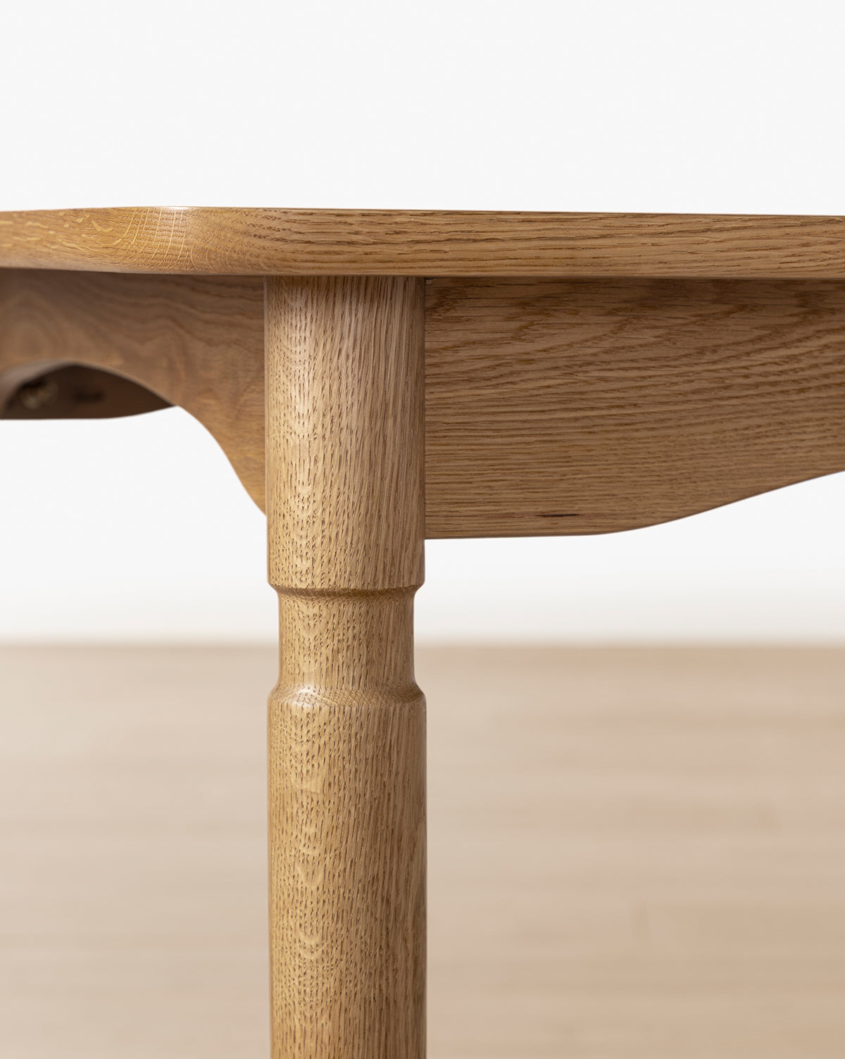 Close-up of the Phipps Dining Table leg and tabletop edge, highlighting natural wood grain and expert craftsmanship against a plain, light-colored floor and wall, by McGee & Co.