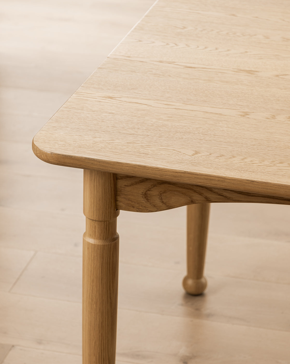 Close-up of the Phipps Dining Table’s corner, featuring rounded edges and turned legs, set on a matching light wood floor by McGee & Co.