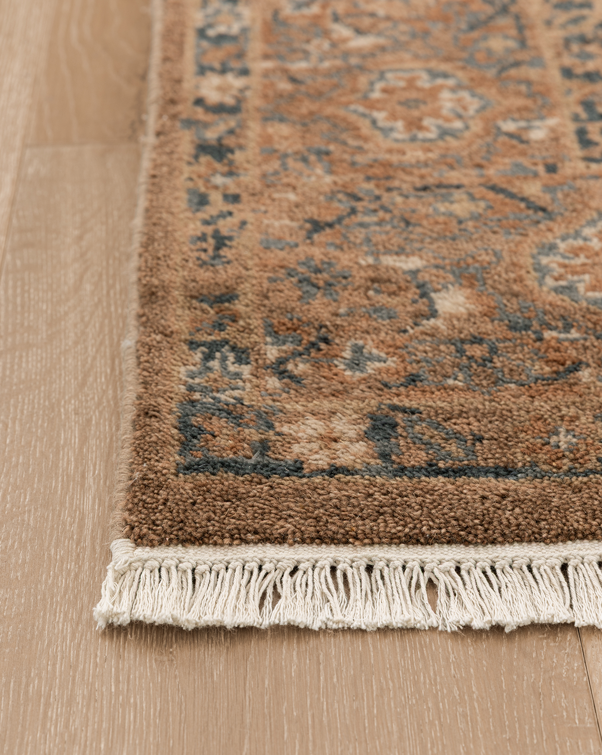 A close-up of the Piedmont Hand-Knotted Wool Rug highlights its blue and brown patterns, beige fringe, and artisanal details, beautifully displayed on a light wood floor, by McGee & Co.