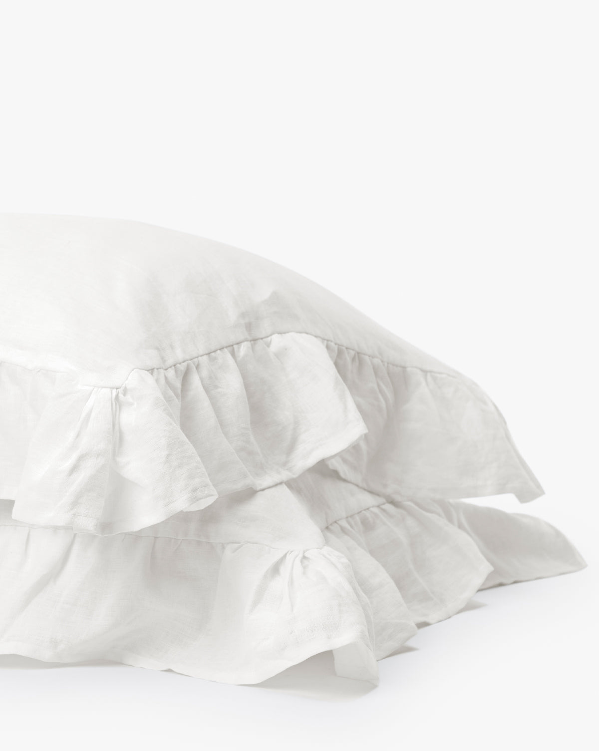 The Ruffle White Linen Shams (Set of 2) are stacked against a plain white background, showcasing the elegance of their ruffled edges and pure linen fabric.
