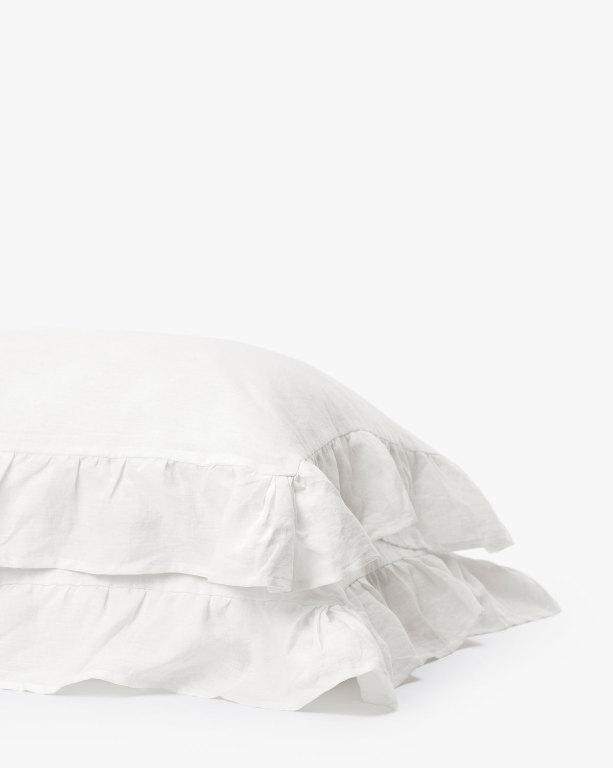 The Ruffle White Linen Shams (Set of 2) are stacked against a plain white background, highlighting the timeless elegance of these 100% linen pillow shams with ruffled edges.
