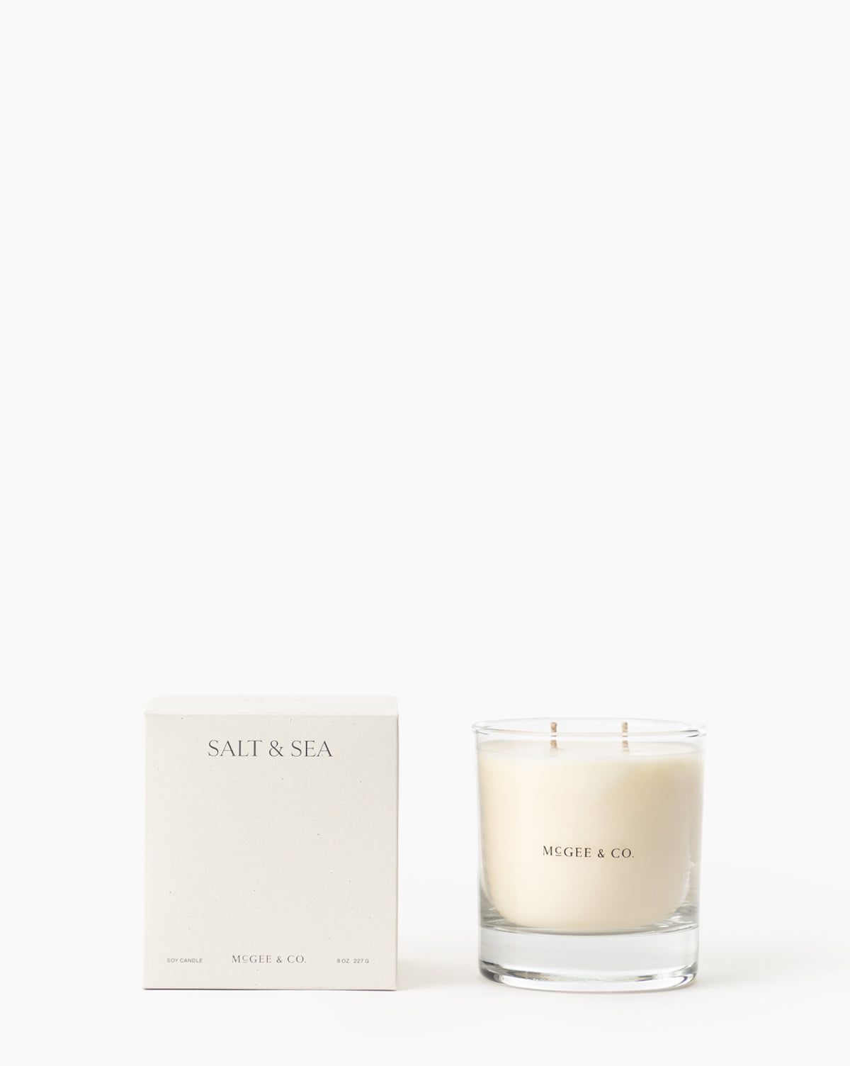 A minimalist white soy wax Salt & Sea Candle in a clear jar sits beside its box, both labeled and displayed against a plain white background, by McGee & Co.