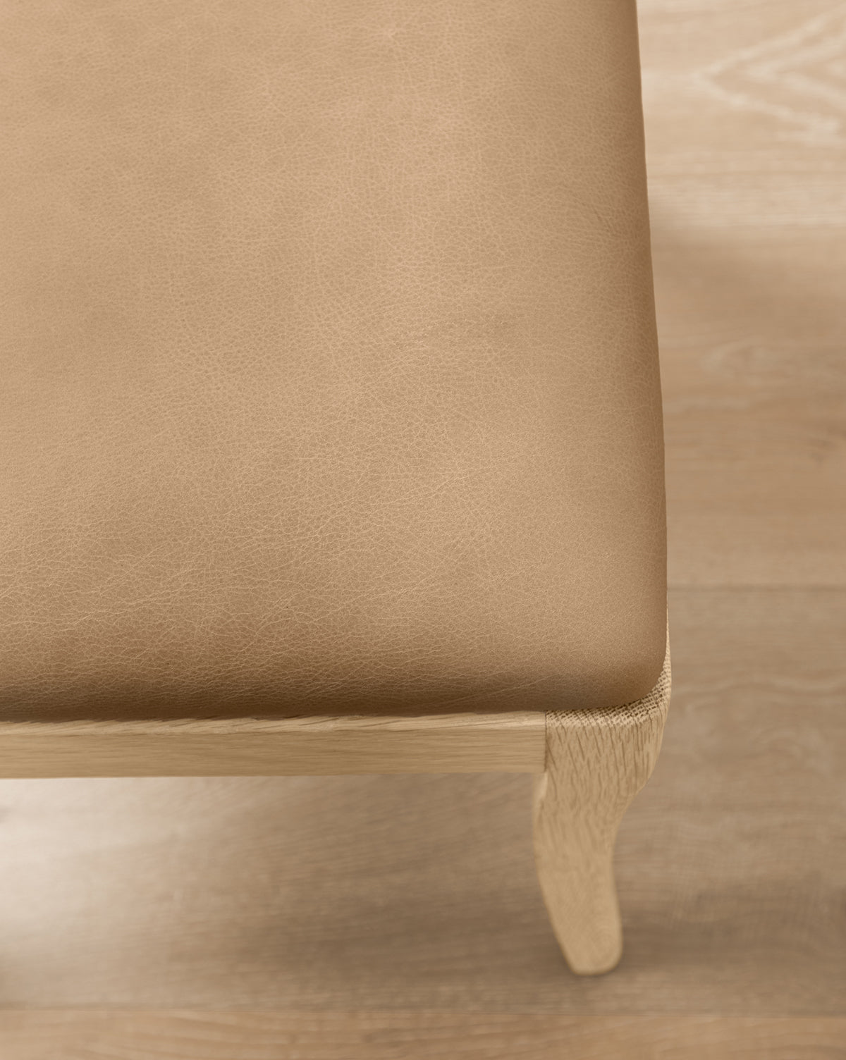 Close-up of the Shepherd Dining Chair’s corner, showing its light brown leather seat cushion and sturdy white oak frame on a light wood floor by McGee & Co.