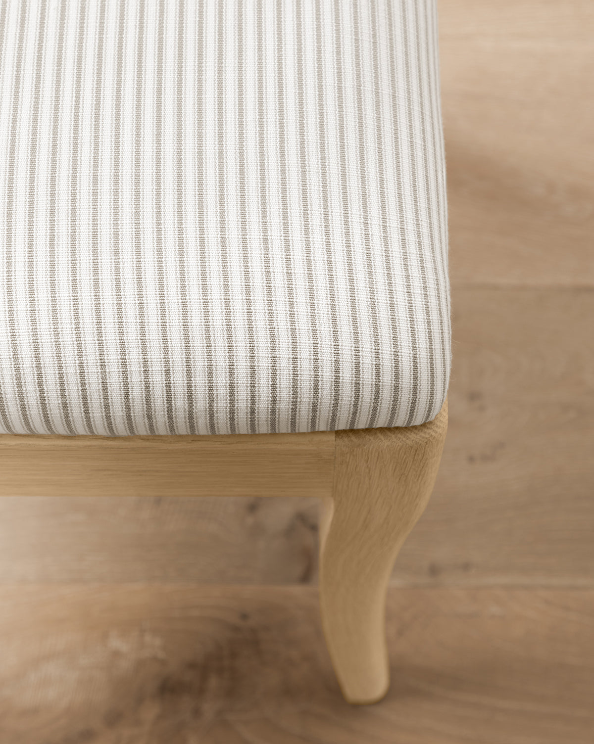 A close-up of the Shepherd Dining Chair highlights its light-striped upholstered seat and sleek white oak frame, set on a light wood floor, by McGee & Co.