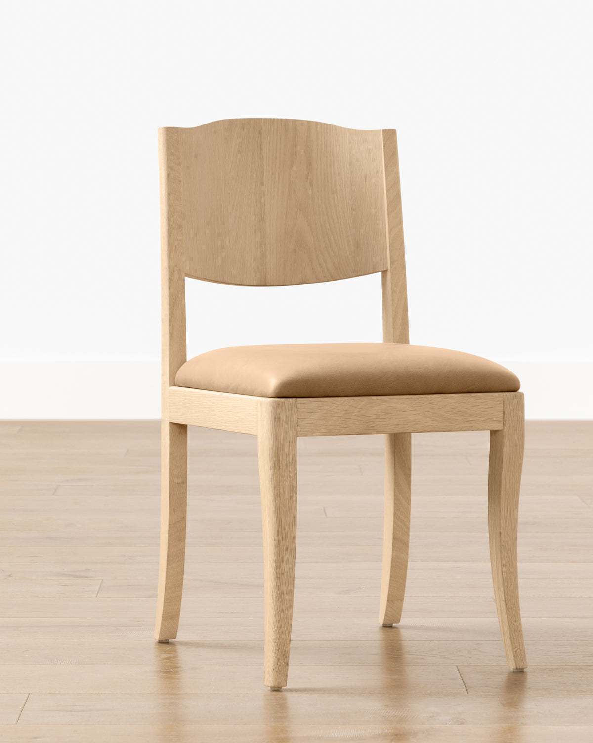 The Shepherd Dining Chair, featuring a white oak frame and a tan upholstered seat cushion, is placed on a light wood floor with a plain white wall in the background, by McGee & Co.