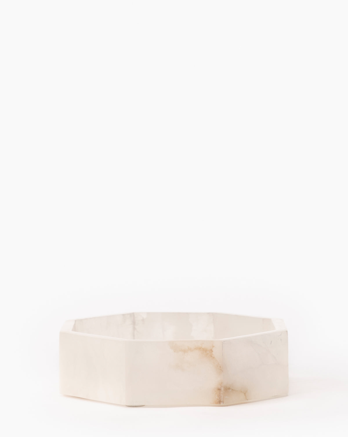 The Sonya Alabaster Box is a hexagonal, shallow bowl crafted from white marble with subtle brown veining, set against a plain white background.