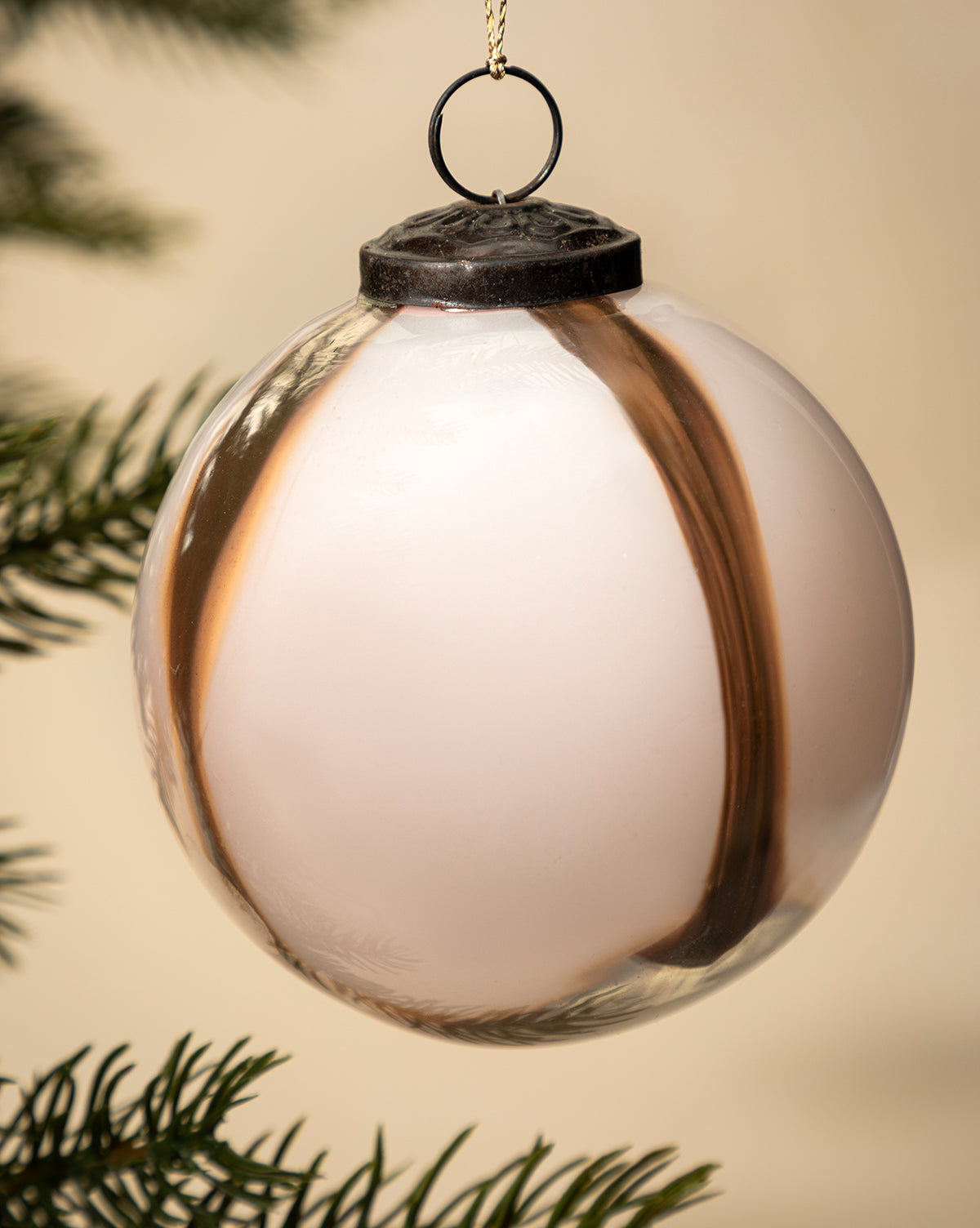 A close-up of the 4" Striped Glass Bauble in white and brown, hand-blown and hanging on a holiday tree branch with blurred green needles in the background, by McGee & Co.