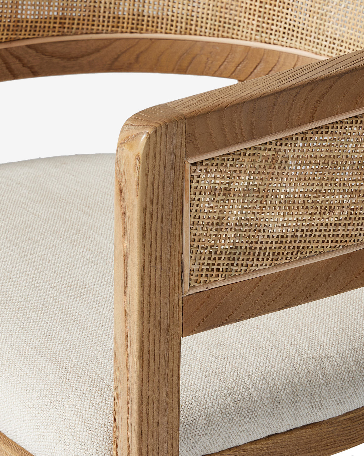 Close-up of the Valissa Dining Armchair, showcasing its light wooden frame, woven cane seatback and armrests, plus an off-white cushioned seat. Set against a white background to highlight its modern design by McGee & Co.