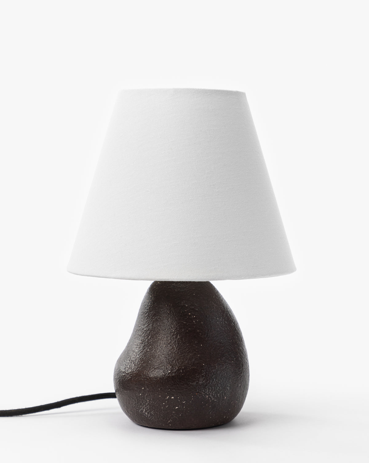 The Vedruna Table Lamp features a brown ceramic base with a smooth, irregular shape and a tapered white shade, displayed against a plain white background by McGee & Co.