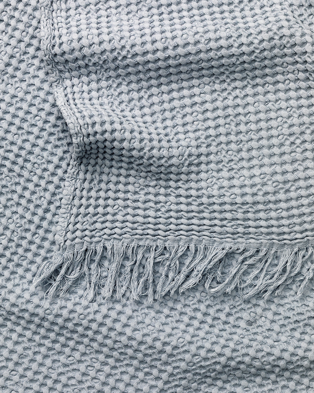 A close-up of the Viola Throw reveals its light gray woven fabric with a textured honeycomb pattern and fringed edges, accentuating the throw’s artisanal charm, by McGee & Co.