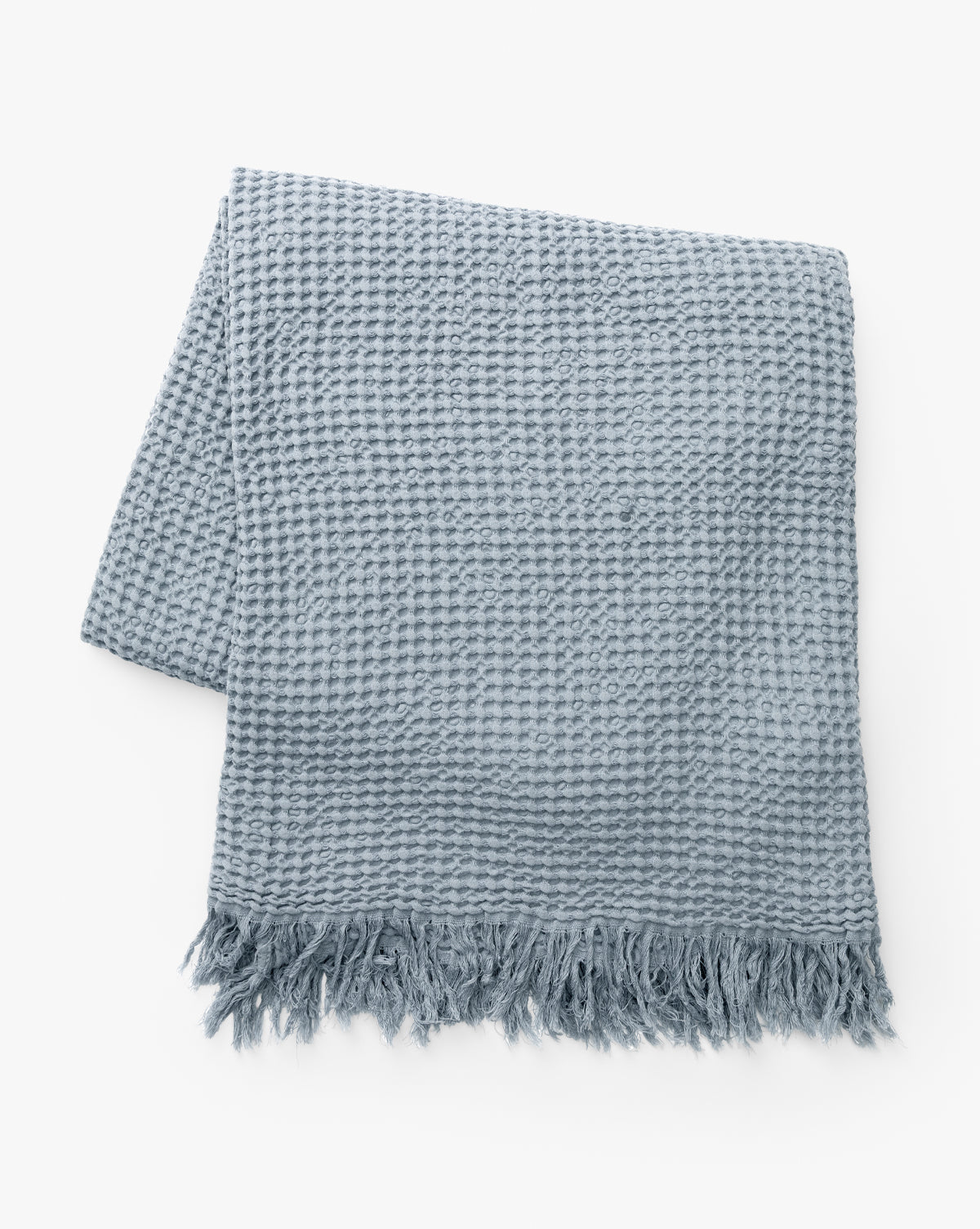 The Viola Throw is a neatly folded artisanal blanket in light blue, featuring a textured weave and fringed edges, displayed on a white background, by McGee & Co.