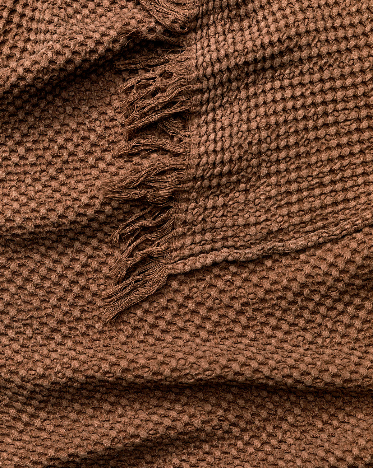 A close-up of the Viola Throw highlights its textured brown waffle pattern and fringe edge, showcasing the soft material and intricate details of this artisanal blanket, by McGee & Co.
