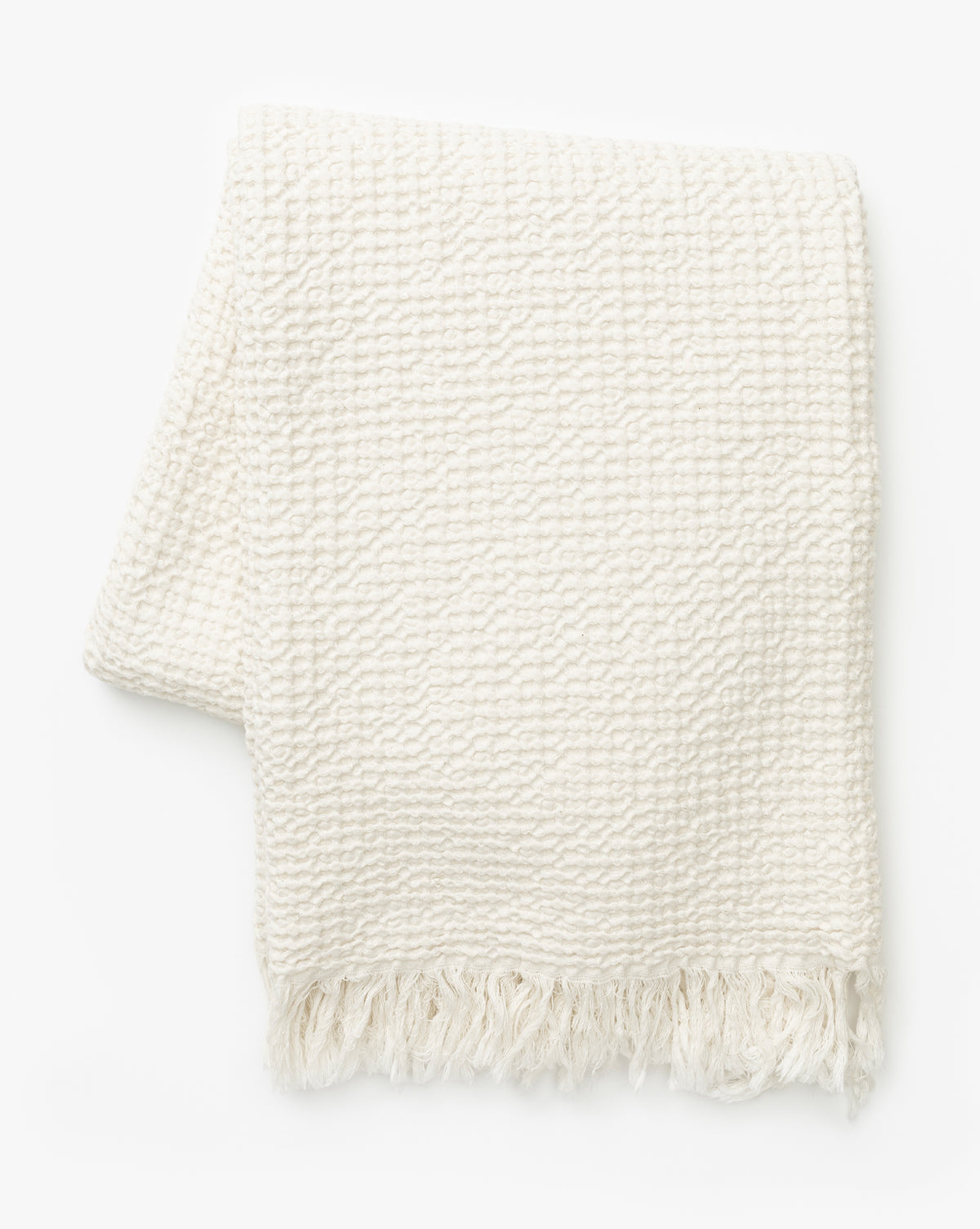 The Viola Throw is a soft, off-white blanket with a waffle textured weave and fringe on the bottom edge, shown against a white background, by McGee & Co.