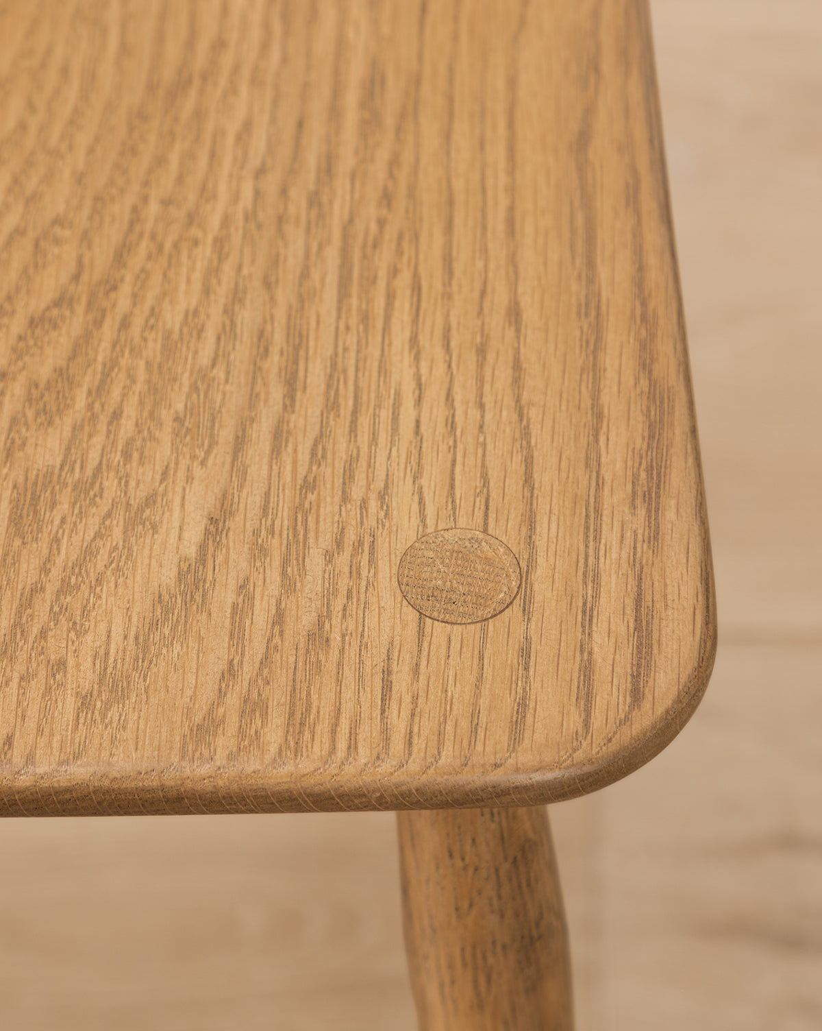Close-up of a solid oak table corner with a round wooden plug highlights the natural grain and smooth finish—an ideal accent for any dining space, perfectly pairing with the Whittaker Chair, by McGee & Co.