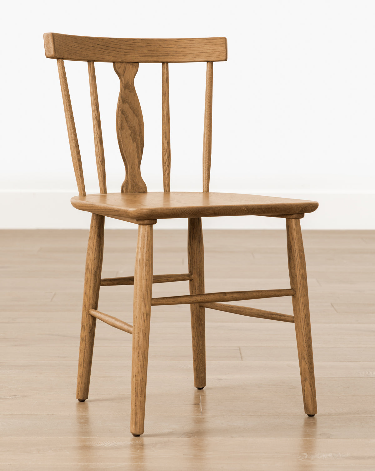 The Whittaker Chair is a solid oak dining chair with a curved backrest, three vertical slats (one carved and wider), a flat seat, and four straight legs—an ideal addition to any dining space, by McGee & Co.