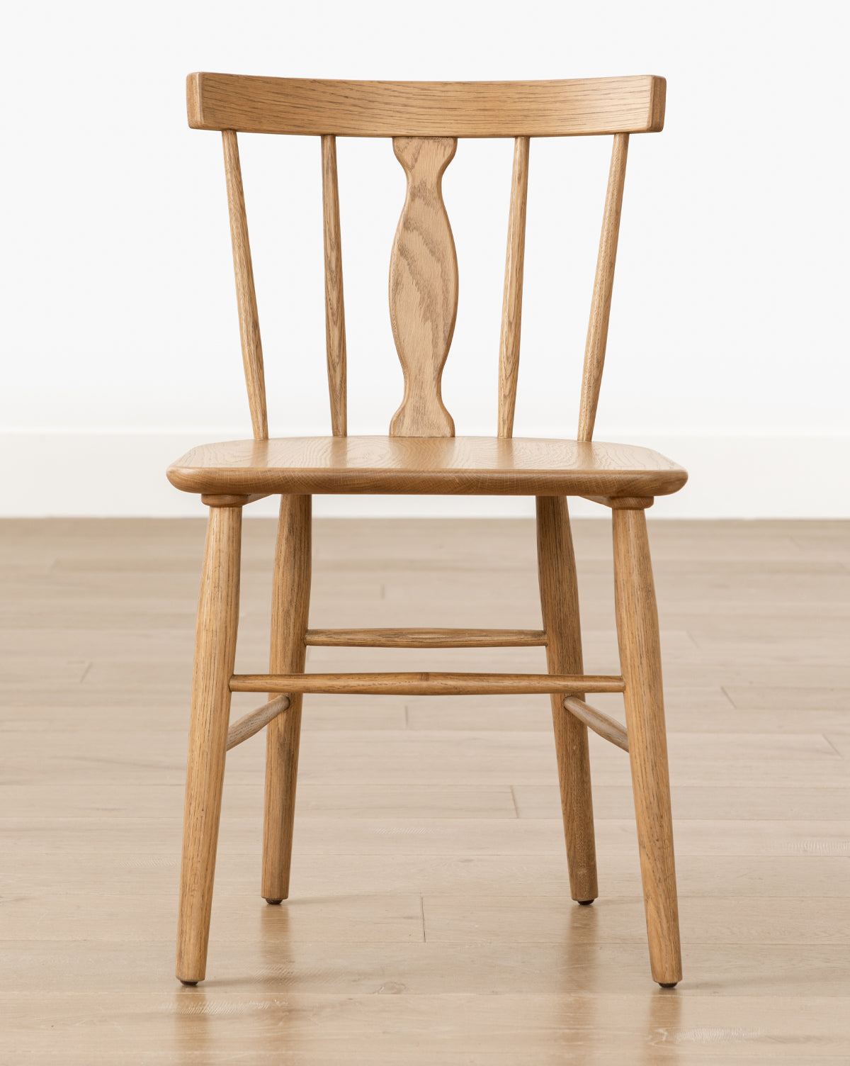 The Whittaker wooden dining chair with a spindle back design, placed in a corner of a room with a light interior, decorated with framed decorative plates on the wall in the background.