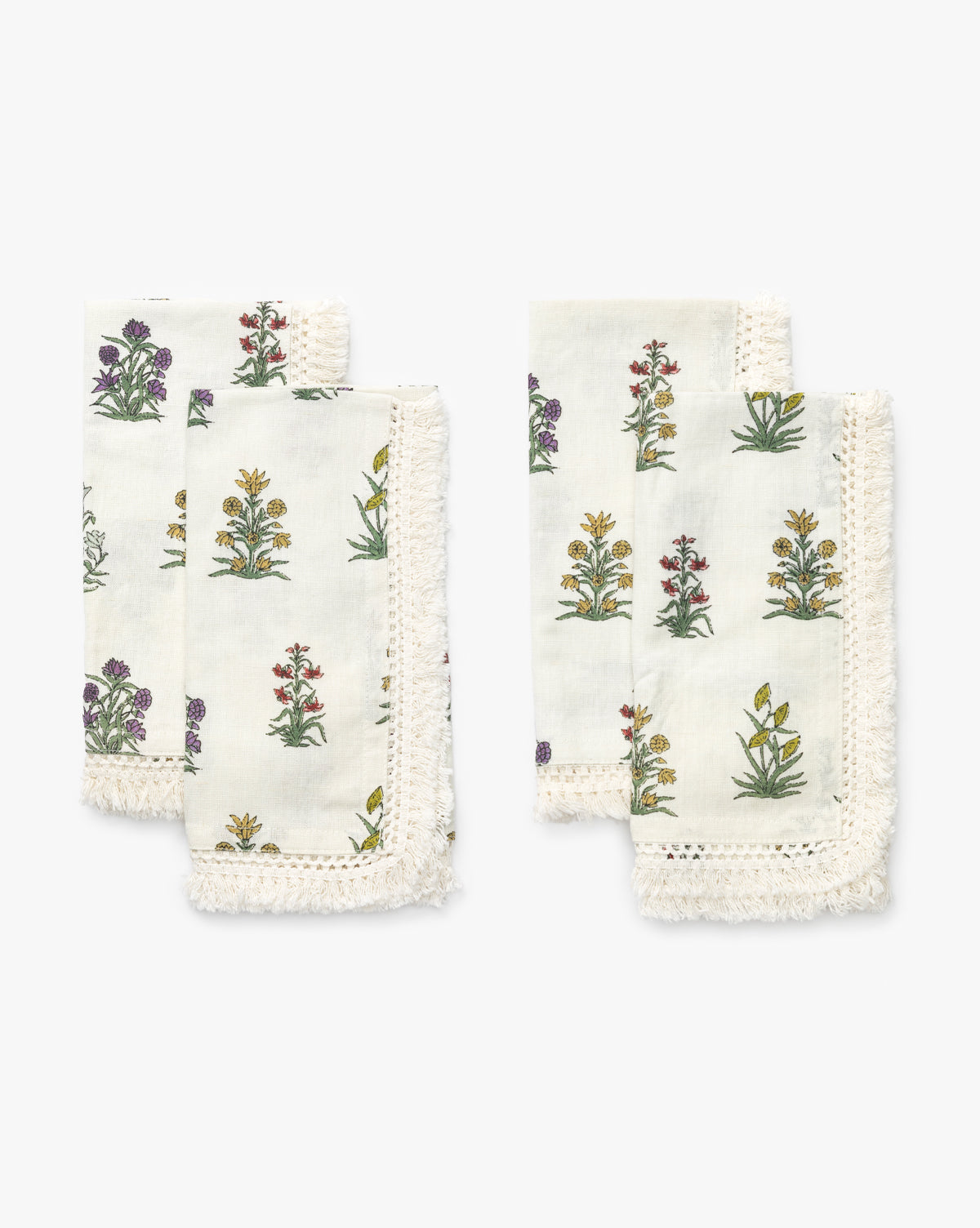 A set of four Wilkie Floral Napkins, crafted from soft cotton with colorful floral block-print-inspired designs and fringed edges, are arranged in two stacks on a white background by McGee & Co.