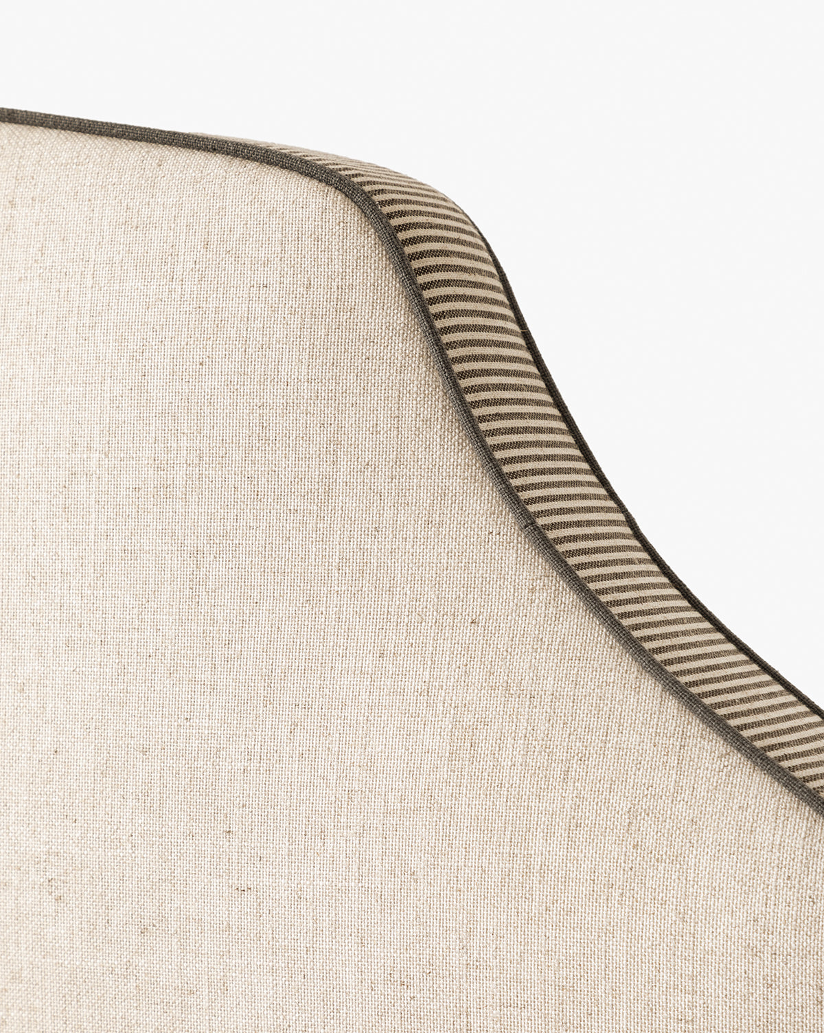 Close-up of the Willoughby Bed with beige linen upholstery, curved top, and striped brown-beige trim. Set against a white background, it features elegant English Oak legs, by McGee & Co.