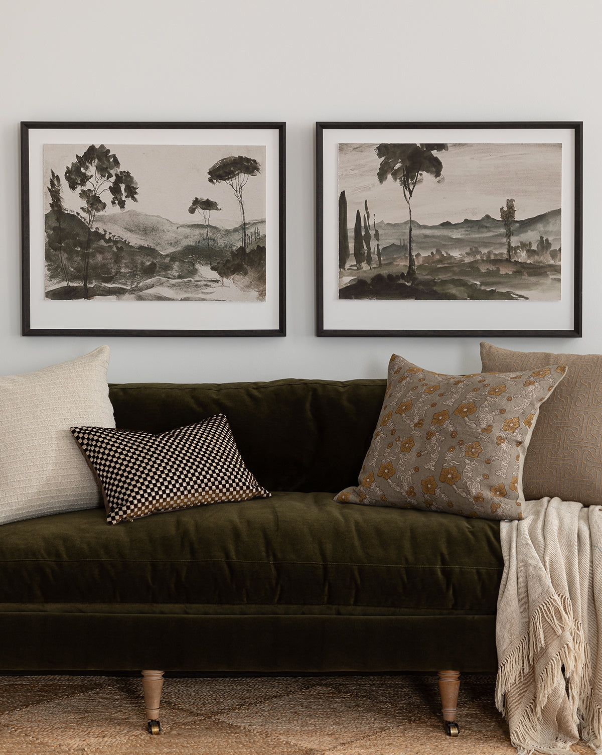 A green velvet sofa with assorted pillows and a beige throw sits beneath Washed Terrain I, a watercolor art print in a black frame on a white wall.