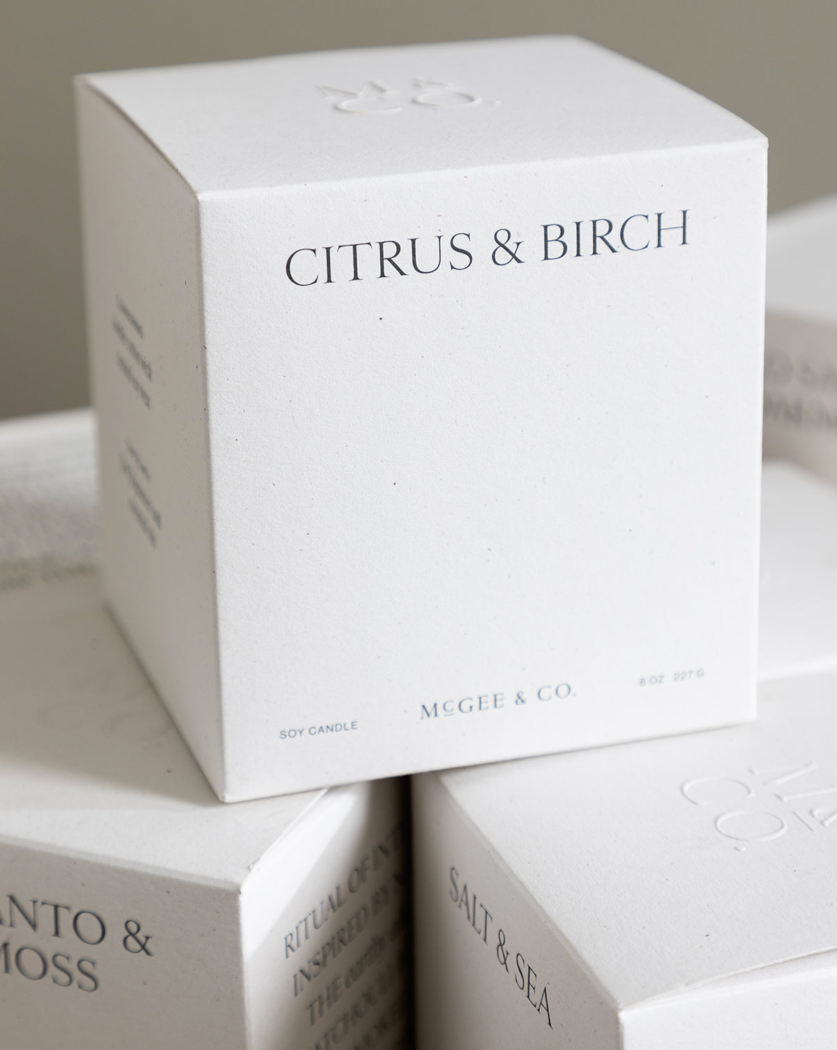 A close-up of the minimalist Citrus & Birch Candle box, crafted from soy wax, with other luxury candle boxes partially visible in the background, by McGee & Co.