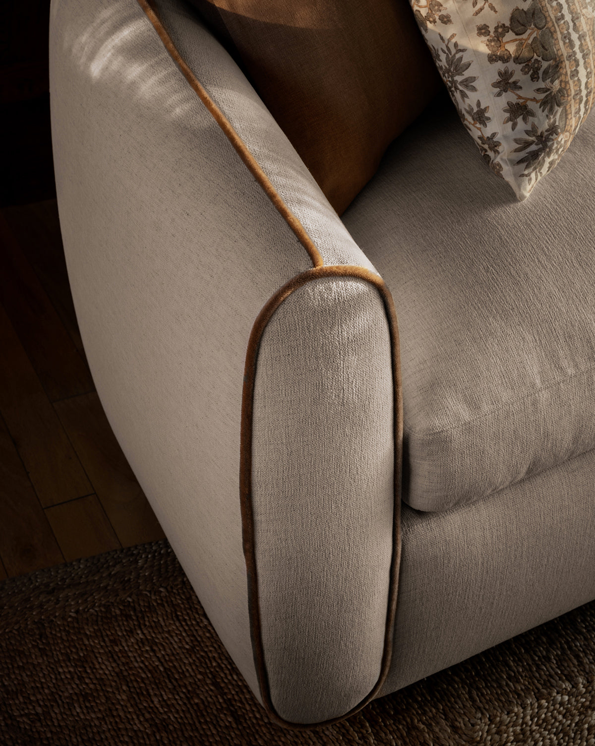 A close-up of the Wexler Sofa 90 in light beige with brown piping, featuring a patterned cushion and textured rug on a wooden floor, by McGee & Co.