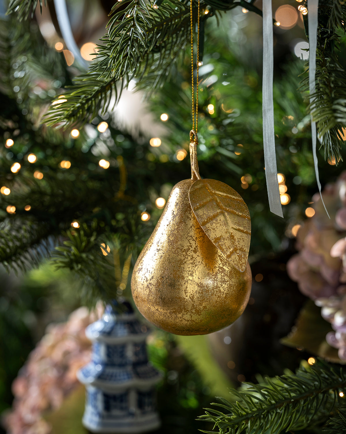 The Gilded Pear Ornament, featuring a leaf detail, hangs on a Christmas tree among pine needles and warm white lights, capturing the nostalgic charm of a vintage holiday decoration, by McGee & Co.