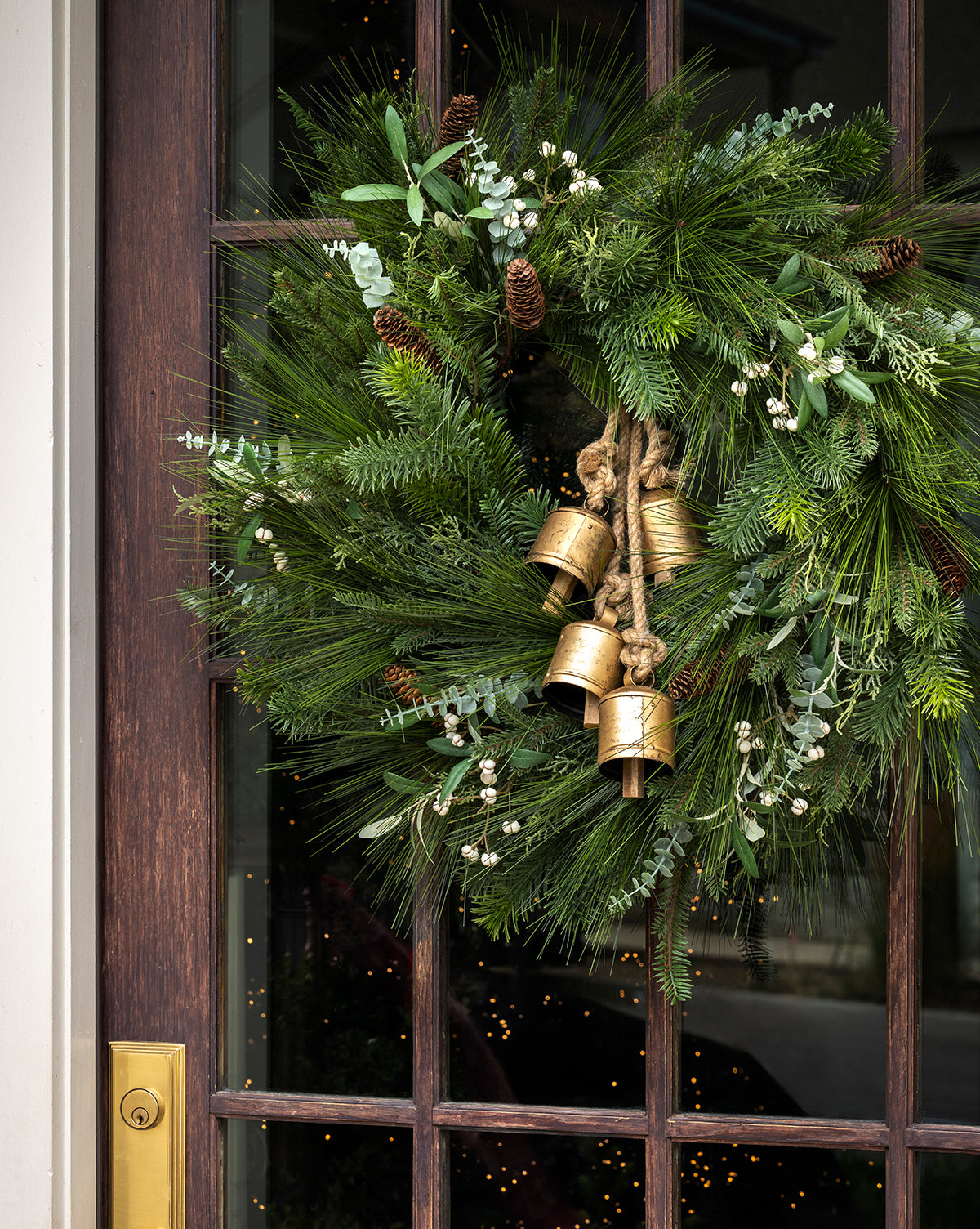 The 24" Pinecone & Berries Faux Wreath features pine needles, pinecones, white berries, and three gold bells tied with rope at the center—perfect festive decor for your door, by McGee & Co.