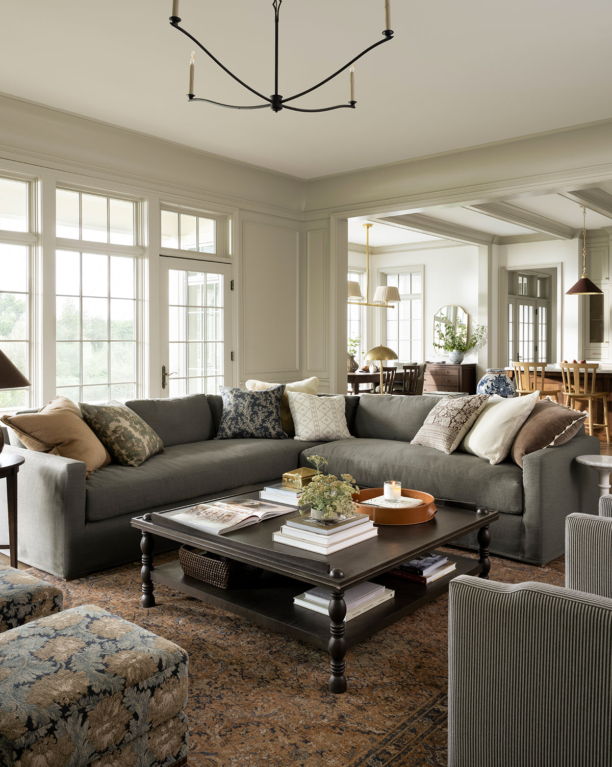 A spacious living room features a large gray sectional, patterned pillows, and dark wood coffee table atop the Piedmont Hand-Knotted Wool Rug. Natural light pours in from large windows, with the dining area visible in the background, by McGee & Co.